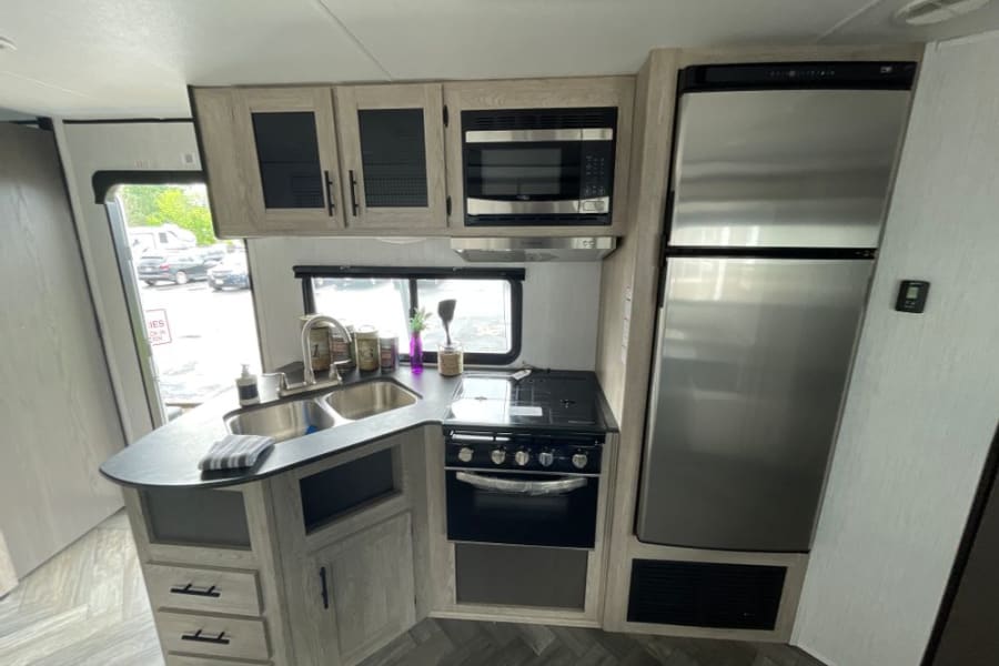 Modern RV rental kitchen interior featuring stainless steel appliances: fridge, stove, microwave, and double sink.