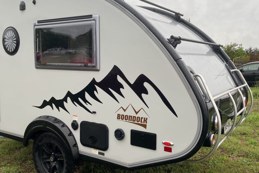 Explore the outdoors with this Boondock teardrop RV rental trailer. A rugged camper ready for adventure, parked on grass.