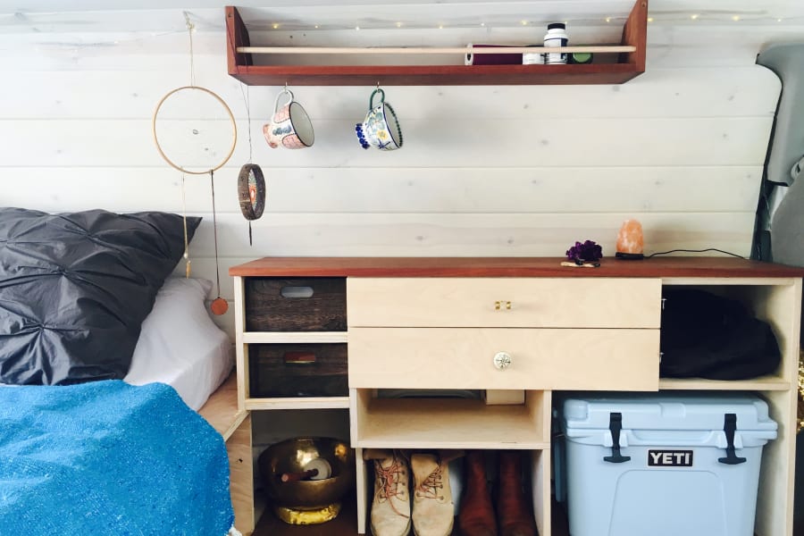 This RV rental features a cozy bed, custom storage with a Yeti cooler, and ambient lighting for your journey.