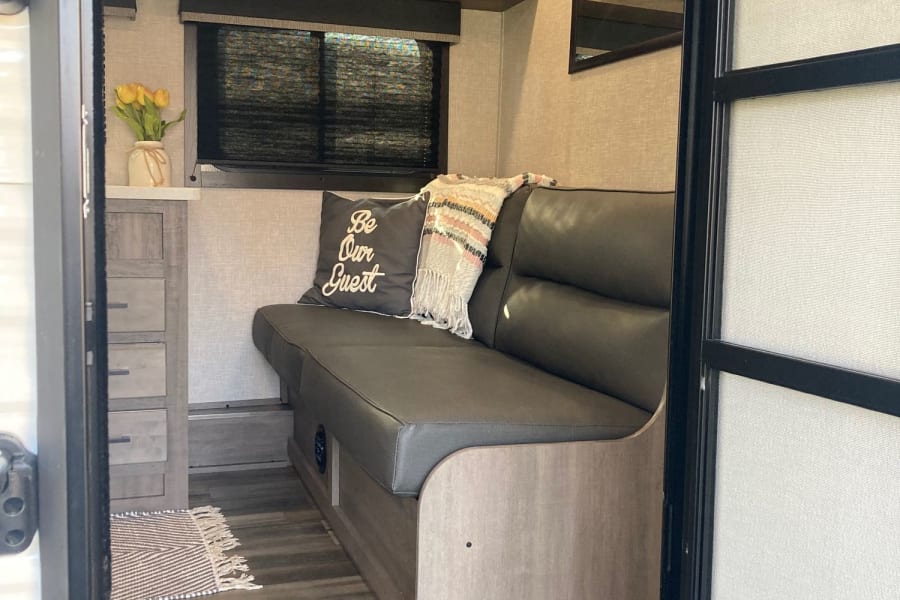 Step into a warm rv rental: a cozy living area with a dark gray dinette, overhead cabinets, and wood-style floor.