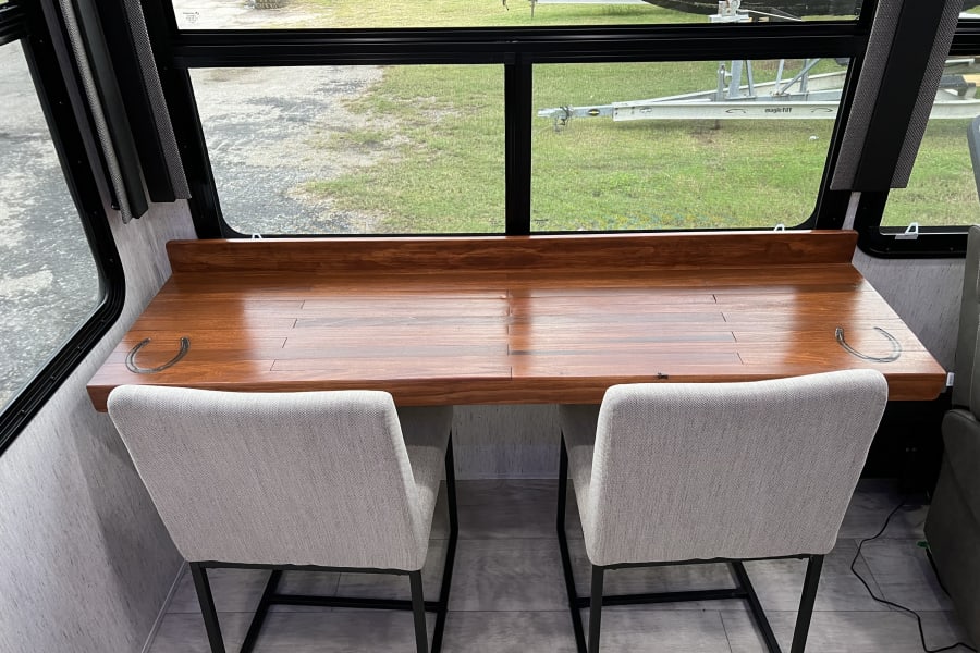 RV rental: Bright RV interior with a wooden desk, unique horseshoe handles, two chairs, and a scenic view.