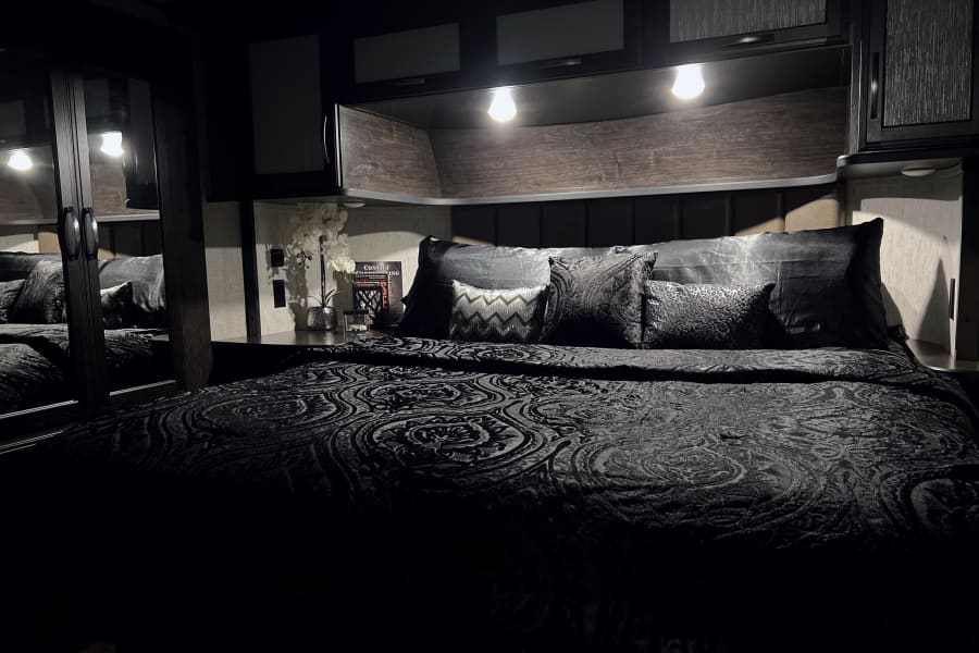 Dark, cozy RV rental bedroom featuring patterned bedding, overhead lights, and modern, inviting decor.