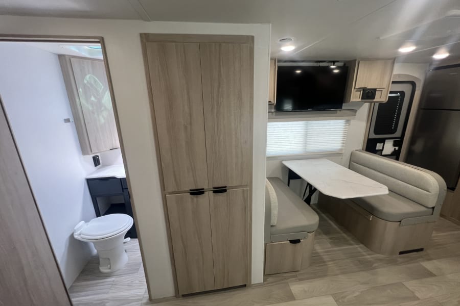 An rv rental interior featuring a bright dinette, TV, refrigerator, and compact bathroom with toilet and sink.