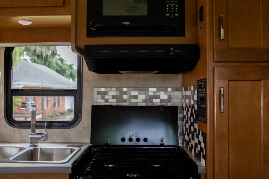 This RV rental kitchen features a microwave, gas stove with oven, double sink, and warm wood cabinets.