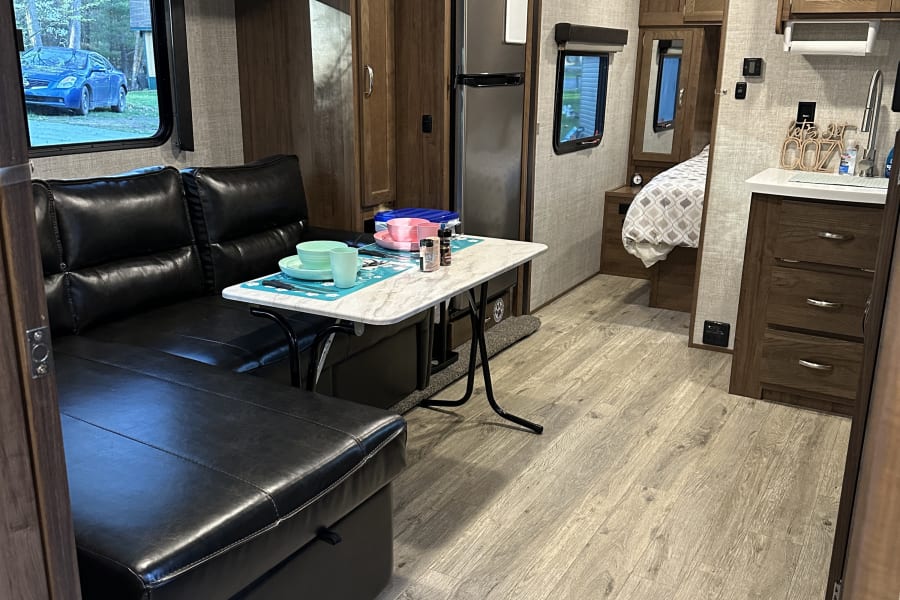 Step inside this RV rental! Bright interior with black leather sectional, dining table, kitchen, and cozy bedroom.