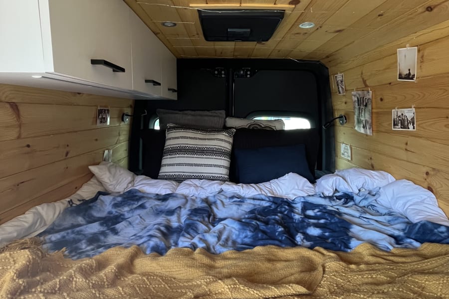 Inviting rv rental sleeping area featuring wood paneling, a comfy bed, and practical overhead cabinets.