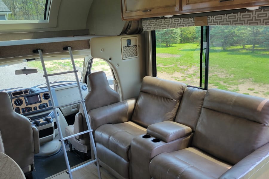 Spacious RV rental interior featuring a driver's cockpit, over-cab bed, and comfortable sofa, ideal for travel.