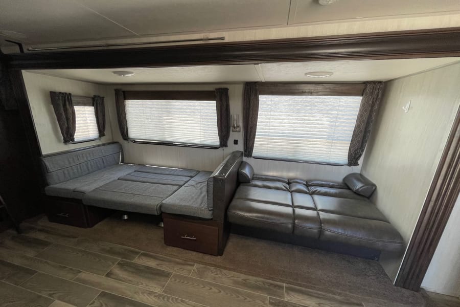 RV rental living area showing two convertible sofa-beds (fabric and leather), windows, and mixed flooring for versatile use.