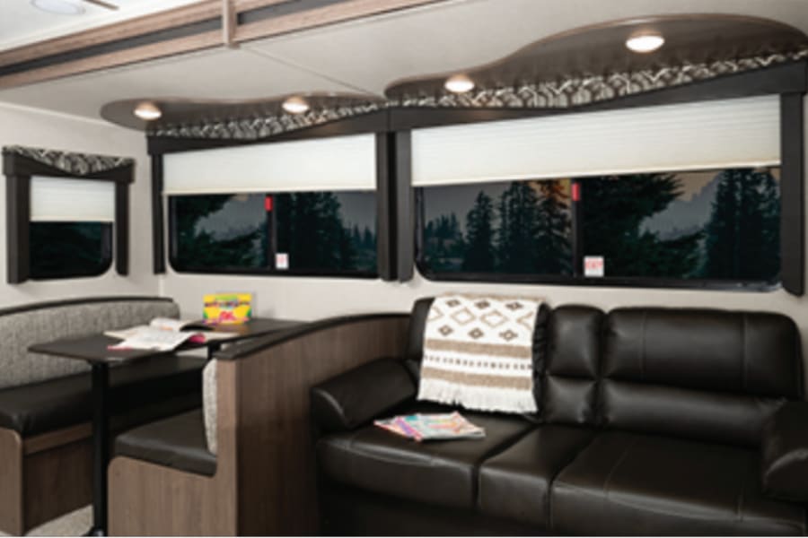 Inside your RV rental: a modern living space with a comfy dinette, sofa, and scenic window views.