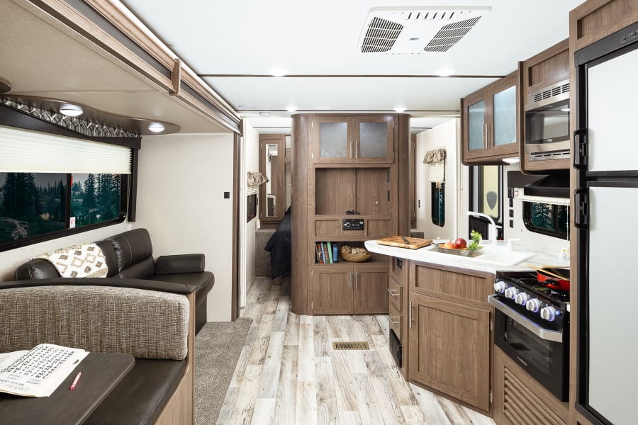 Explore this modern RV rental interior featuring a full kitchen, comfy dinette, and spacious living area. Ideal for adventures!