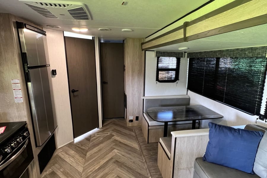 This RV rental interior features a kitchen area with fridge/stove, a dinette, and a sofa lounge. Note the modern herringbone floor.