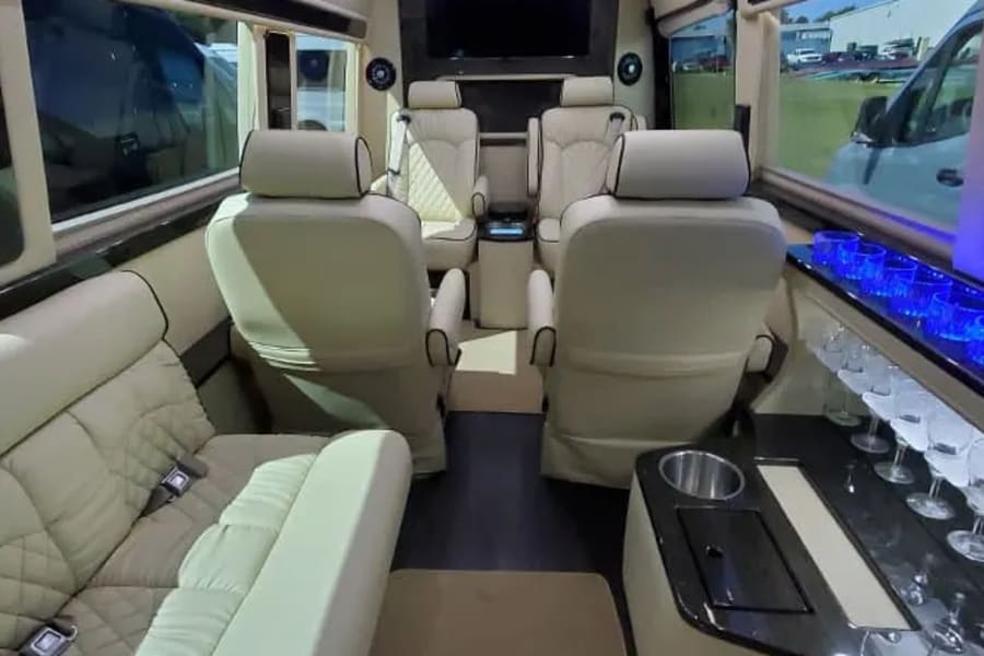 Luxurious RV rental interior: cream leather seating, large TV, and bar with blue lighting. Perfect for travel.