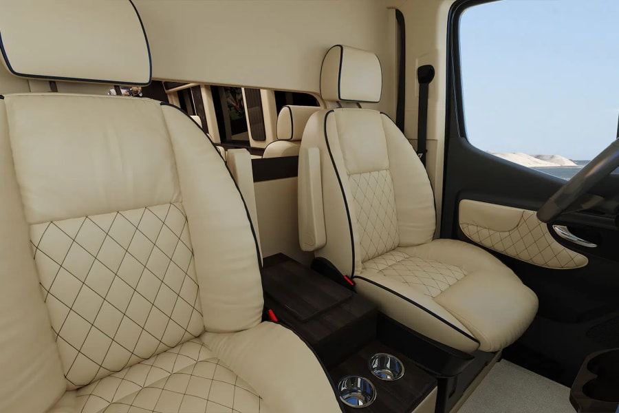 Luxurious RV rental interior with cream leather diamond-stitched captain's chairs, cupholders, and a view of desert dunes.