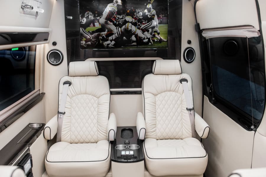 Luxurious RV rental interior with plush seats & large TV showing football, perfect for travel comfort.