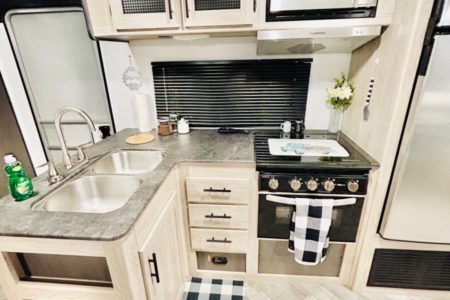 Clean, modern kitchen in an RV rental, featuring a double sink, microwave, stove, and light wood cabinetry.