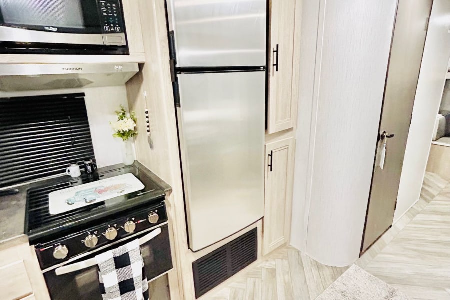 Modern rv rental kitchen. Features microwave, stainless fridge, stove, light cabinets, and herringbone flooring.