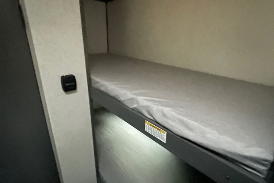 Cozy RV rental bunk beds offer comfy sleeping. Top bunk has a warning label; bottom bunk is visible below.