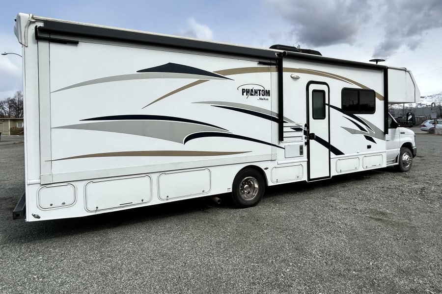 White Phantom by Nexus Class C motorhome with detailed graphics, ready for your next rv rental adventure on a gravel lot.