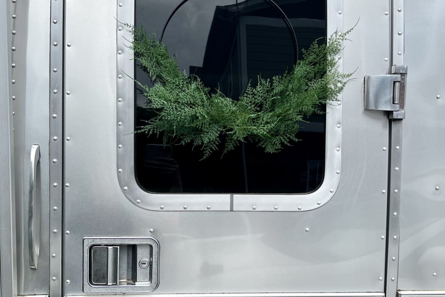 A polished silver Airstream RV door with a window and green wreath. Ideal for your next RV rental adventure.