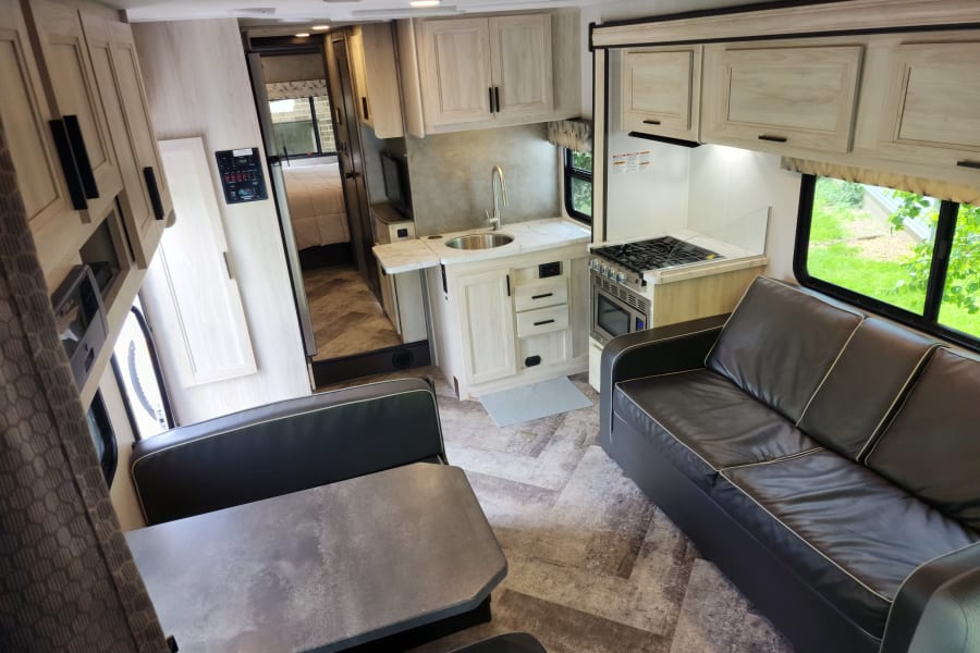 Modern RV rental interior featuring a full kitchen, dining area, comfortable sofa, and hallway to the bedroom, ideal for travel.