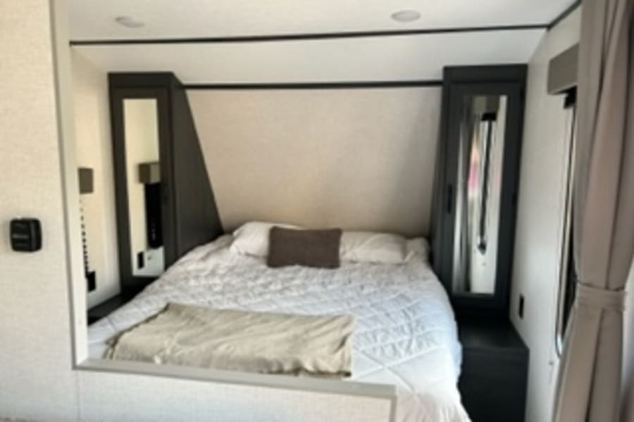 Explore this RV rental bedroom: a cozy bed with crisp white bedding, flanked by mirrored wardrobes. Great for camping trips.