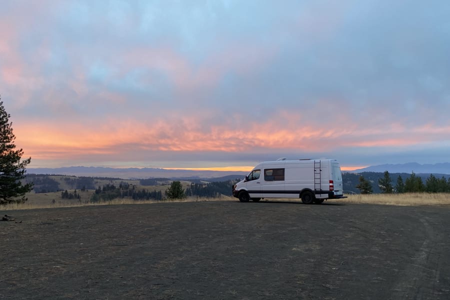 White RV rental van at sunset/sunrise, offering stunning views of mountains and nature for your next adventure.