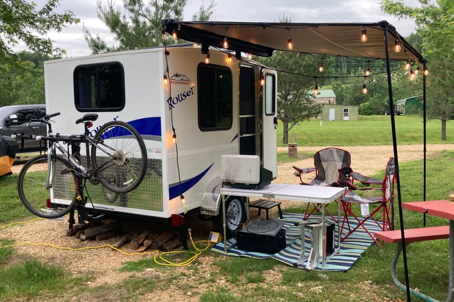 Awning open. Ground mat and camping chairs included, as well as aluminum table and cafe lights!  Camp stove and bike rack are add-ons. 