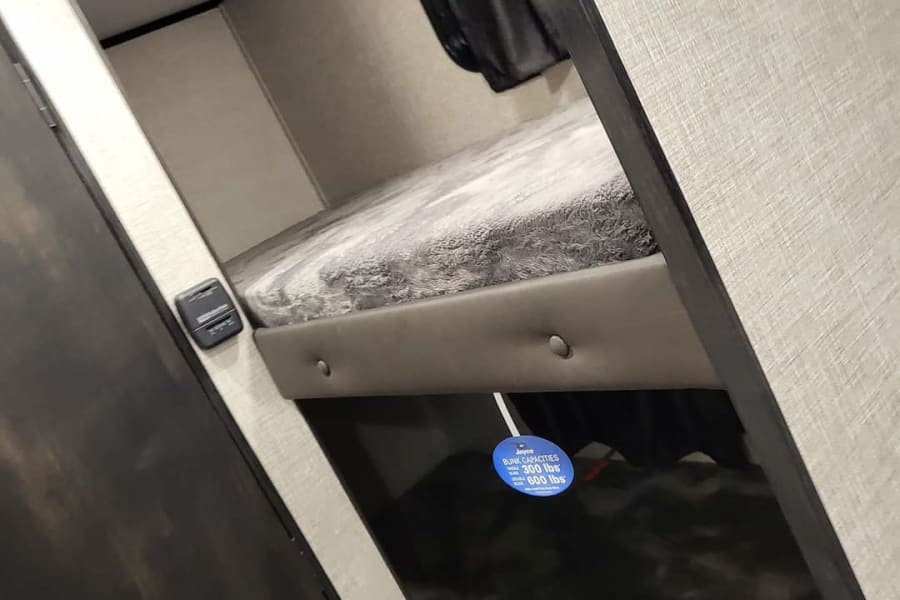 Inside an RV rental: comfortable stacked bunk beds for travel, showing a tag with 300 lbs (upper) and 600 lbs (lower) capacity.
