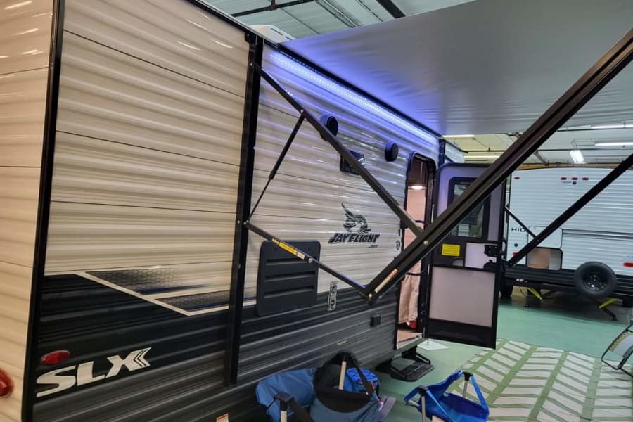 Explore this RV rental: A travel trailer with its lighted awning deployed and door open, ideal for camping.