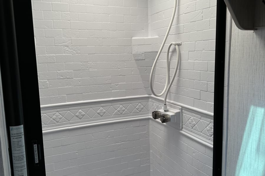 Spacious white-tiled shower in an RV rental, featuring a skylight and a retractable door for compact living.