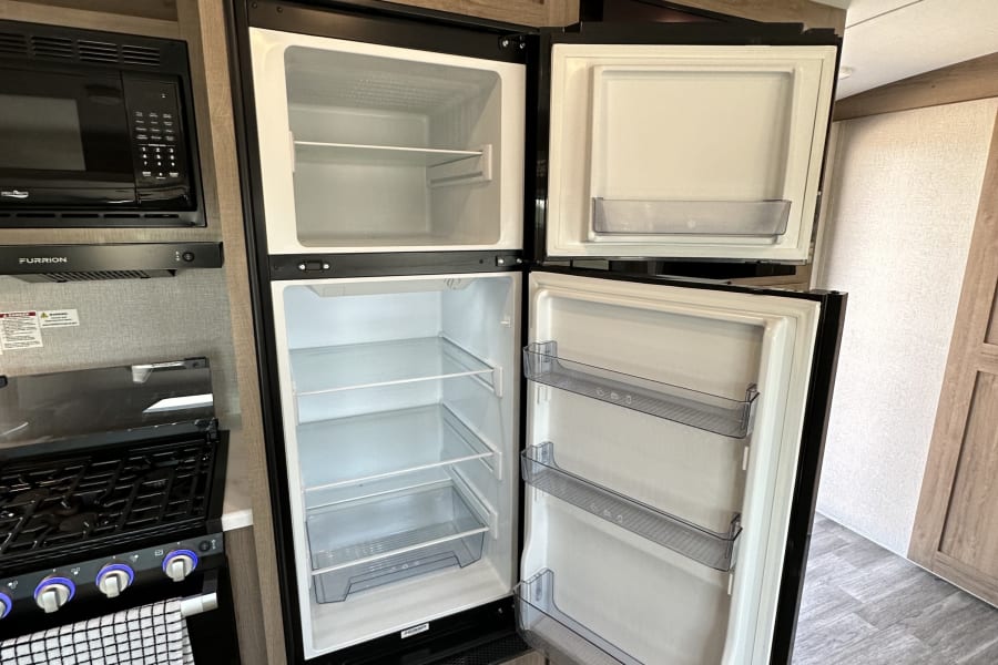 Modern RV rental kitchen with open fridge/freezer, microwave, and gas stove, ready for your adventures.