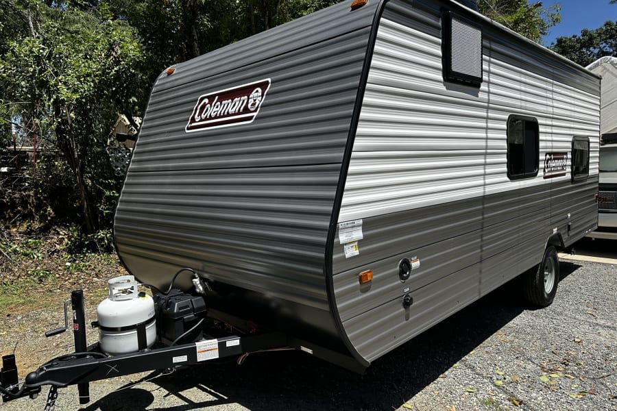 This striped Coleman travel trailer, ideal for an RV rental, is parked on gravel, ready for adventures.