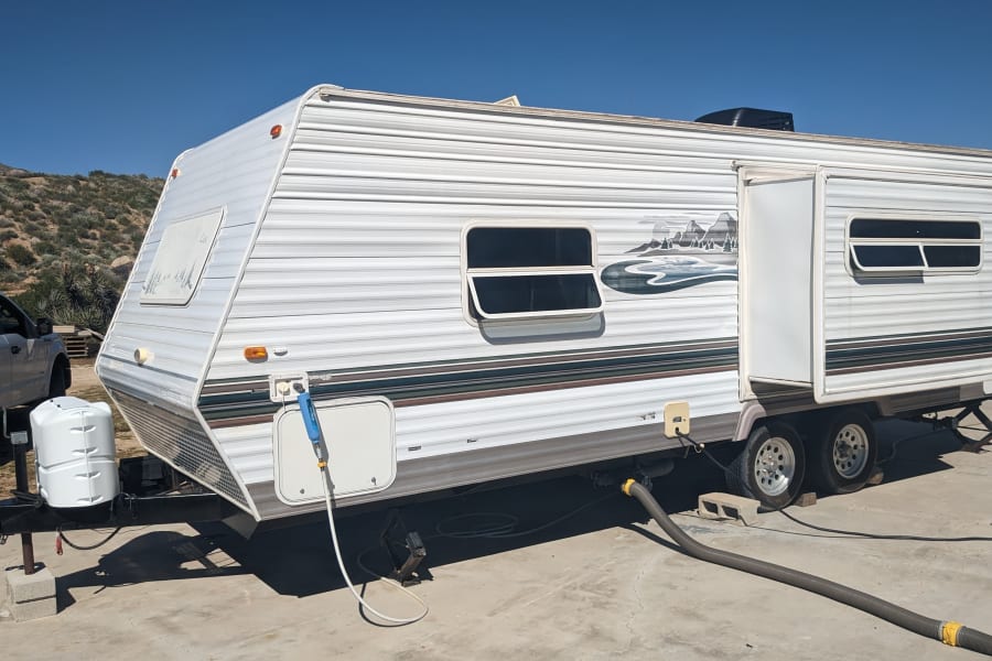 White rv rental travel trailer, fully set up with utility hookups on concrete, ideal for outdoor trips.