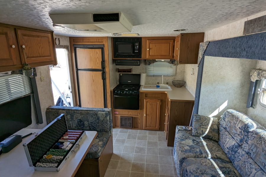 RV rental interior: full kitchen with microwave, fridge, stove, a dining booth with poker chips, and a comfy sofa.