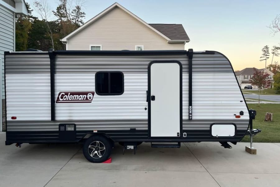 Side view of a striped Coleman travel trailer, ideal for an RV rental adventure, parked on a concrete driveway.
