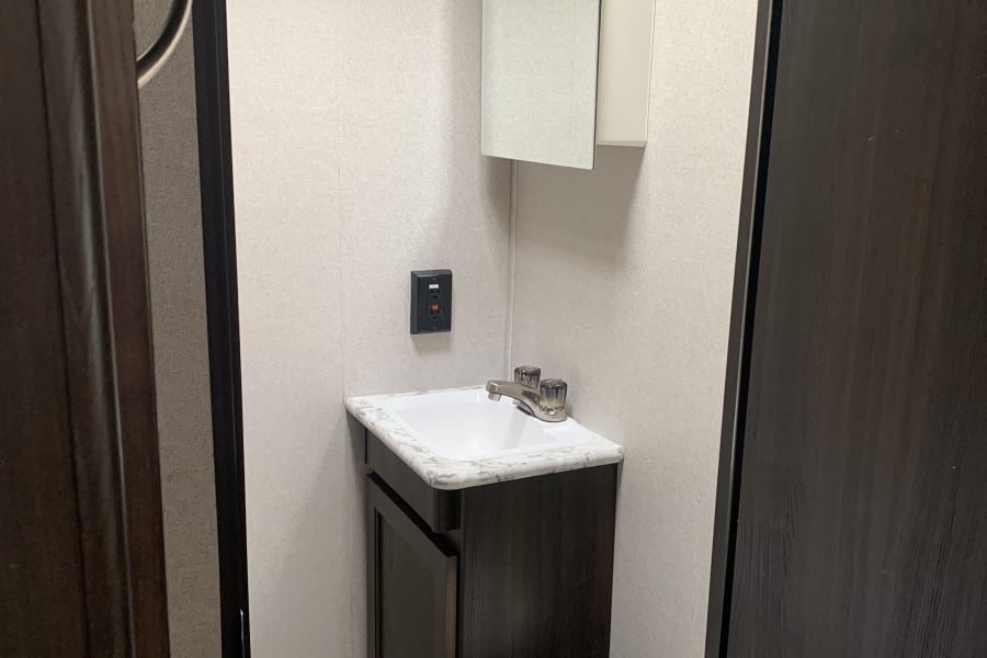 Compact rv rental bathroom: dark vanity with white sink, toilet, and mirrored cabinet visible. Light-colored walls.
