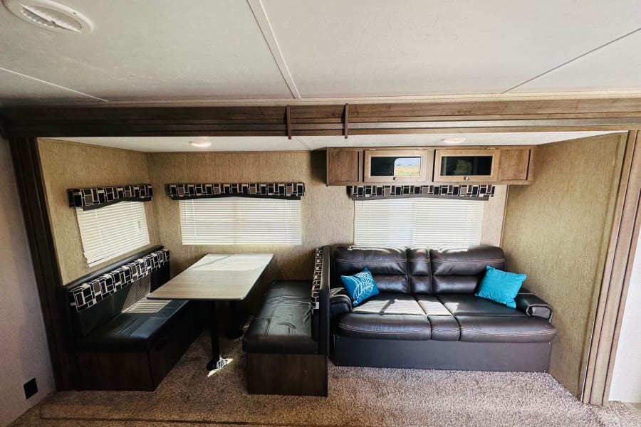 Step inside this cozy RV rental with a dining booth, large sofa, windows, and overhead storage.