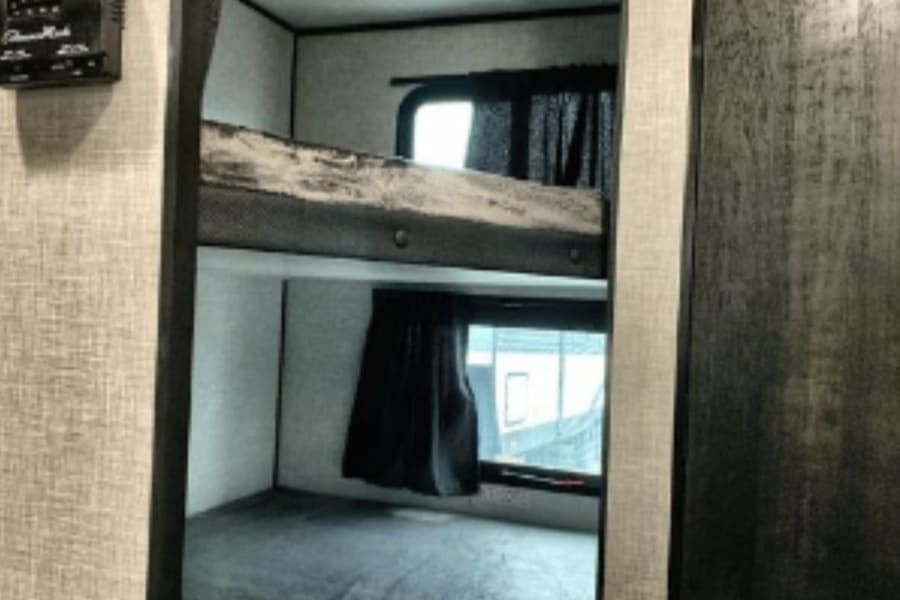 Cozy bunk beds inside an RV rental, perfect for family camping trips. Features windows and a climate control panel.