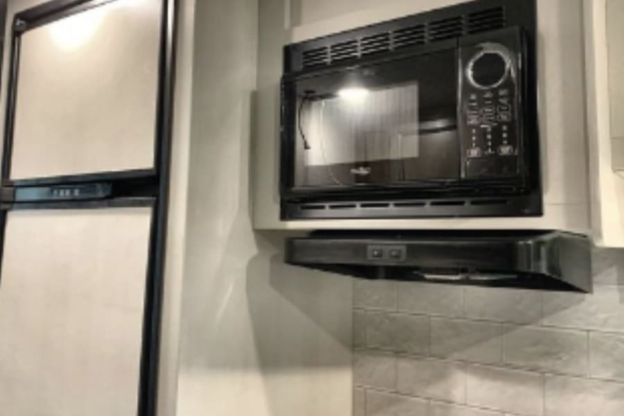 RV rental kitchen featuring a compact refrigerator, an over-the-range microwave, and a ventilation hood.
