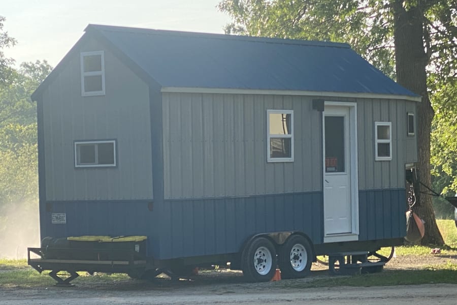 A two-tone (gray & blue) tiny house on wheels, perfect for an RV rental, parked outdoors on a sunny day.