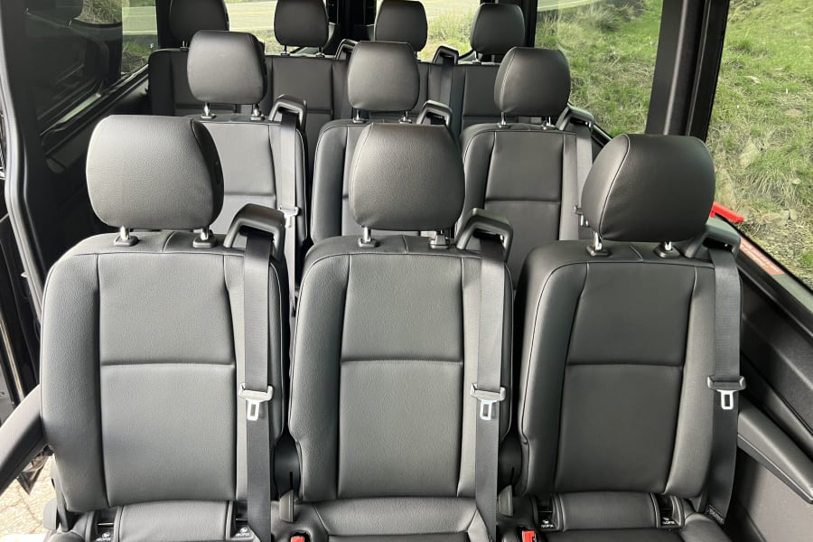 Inside a luxurious RV rental: multiple rows of black passenger seats with safety belts and ISOFIX anchors visible.