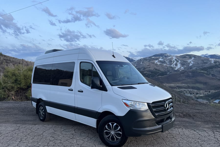 White Sprinter van for RV rental parked on a mountain road with snowy peaks in the background. Scenic view.