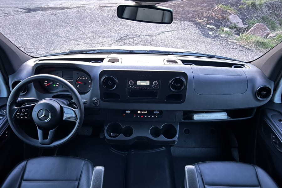 RV rental interior: View from inside a large van's cockpit, showing the dashboard, steering wheel, and road ahead.