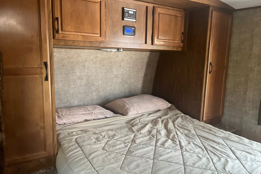 RV rental bedroom with bed, wood cabinets, and solar charge controller mounted above the sleeping area.
