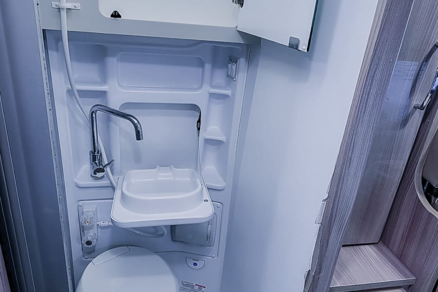 Inside an RV rental, this bright, compact bathroom features a shower, toilet, and fold-down sink.