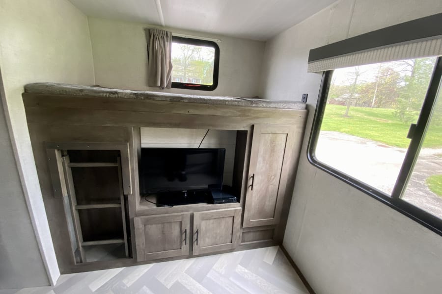 This rv rental features a compact bunkhouse with a comfy bunk bed, TV entertainment, and built-in storage.