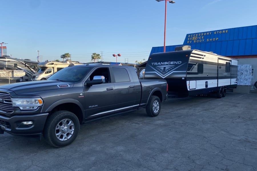 Dark gray Ram 2500 pickup towing a Transcend travel trailer, common for rv rental, parked at an RV service center.