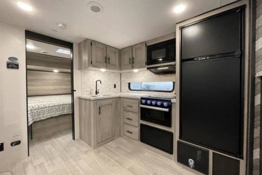 Bright RV rental interior featuring a modern kitchen with appliances and an inviting bedroom area.