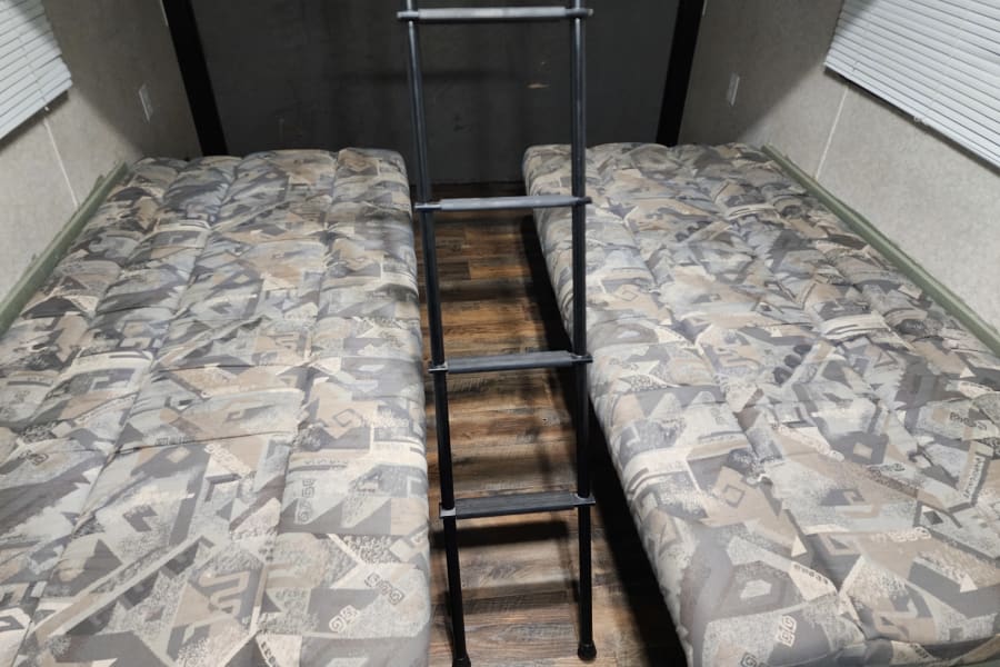 Comfortable RV rental sleeping area with two patterned mattresses and a sturdy ladder in the center.