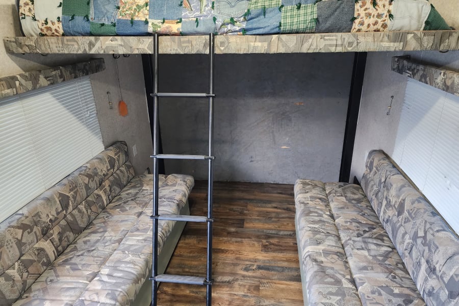 RV rental interior showcasing a bunk bed, two sofas, a ladder, and wood-look flooring for your travels.